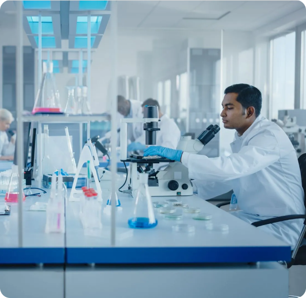 Researcher in a white coat examining samples under a microscope in a bright laboratory
